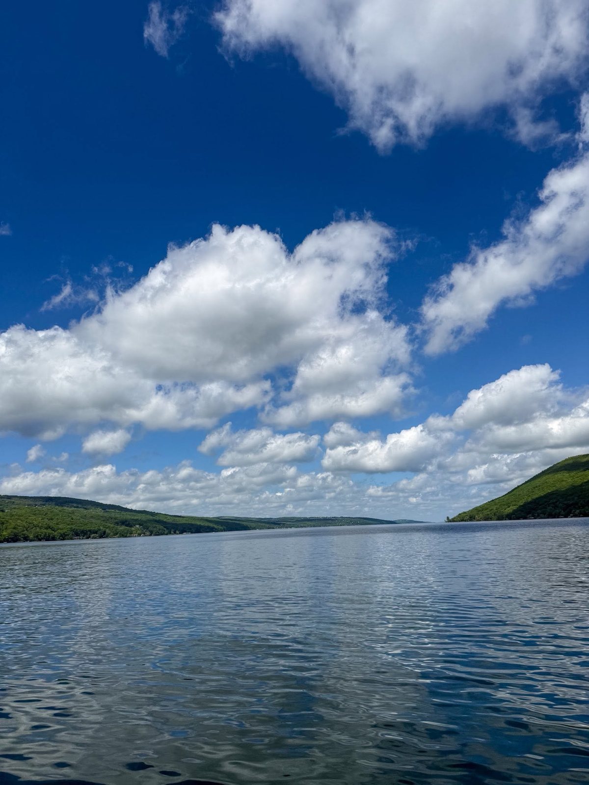 Canandaigua Lake under a blue sky with green hills on both shores